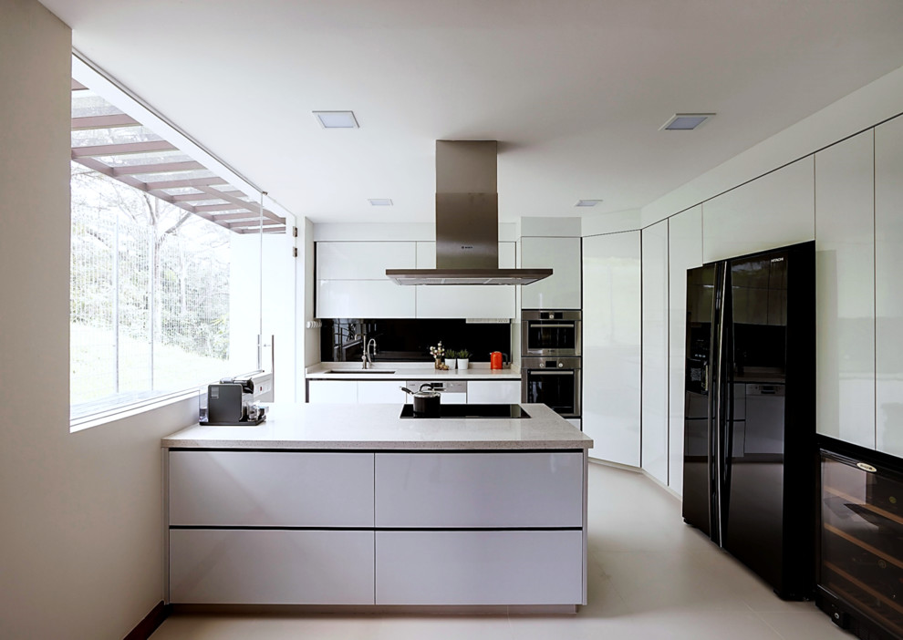 Diseño de cocina lineal minimalista con puertas de armario blancas, encimera de cuarzo compacto, salpicadero negro, salpicadero de vidrio templado, electrodomésticos de acero inoxidable y una isla