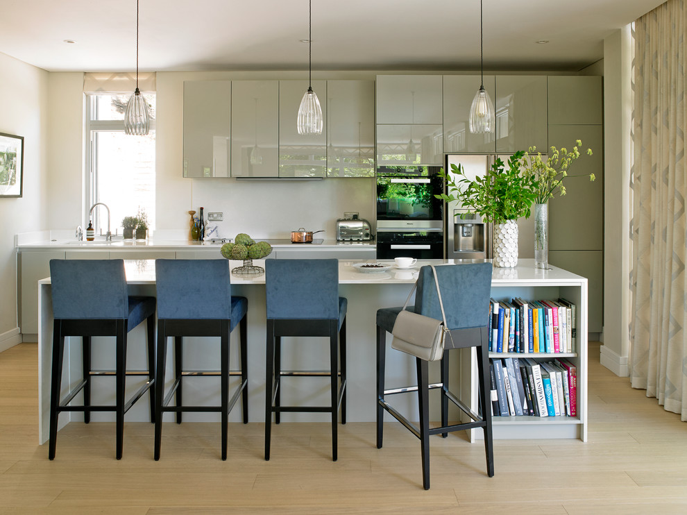 Cette image montre une cuisine design avec un placard à porte plane, des portes de placard grises, un électroménager en acier inoxydable, parquet clair et îlot.