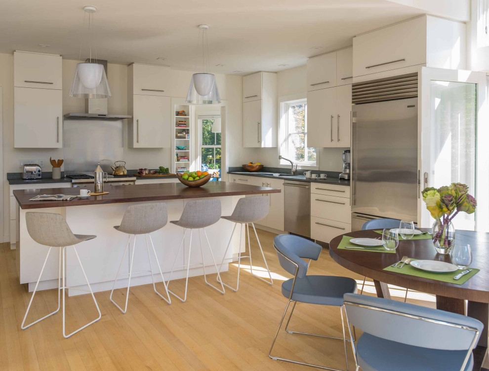 Moderne Wohnküche in L-Form mit flächenbündigen Schrankfronten, weißen Schränken, Küchengeräten aus Edelstahl, hellem Holzboden, Kücheninsel, braunem Boden und grauer Arbeitsplatte in Boston