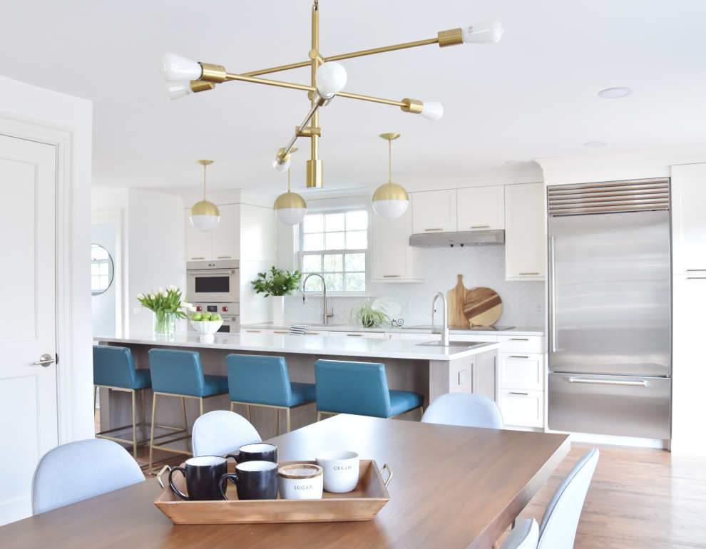 Example of a transitional galley medium tone wood floor and brown floor eat-in kitchen design in Boston with a single-bowl sink, shaker cabinets, quartz countertops, white backsplash, ceramic backsplash, stainless steel appliances, an island, white countertops and white cabinets