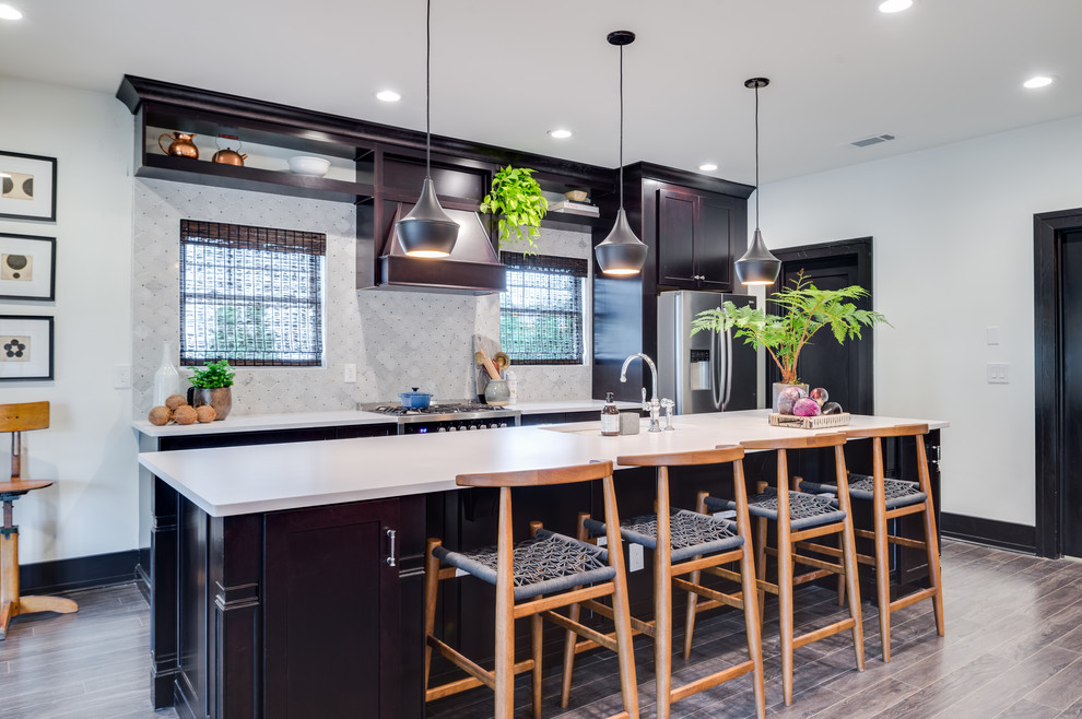 This is an example of a large modern u-shaped kitchen/diner in Nashville with a built-in sink, recessed-panel cabinets, black cabinets, engineered stone countertops, white splashback, ceramic splashback, stainless steel appliances, vinyl flooring, an island and beige floors.