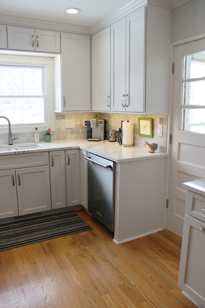 Bild på ett mellanstort vintage vit vitt u-kök, med en undermonterad diskho, släta luckor, vita skåp, bänkskiva i kvarts, grått stänkskydd, stänkskydd i marmor, rostfria vitvaror, ljust trägolv och en halv köksö
