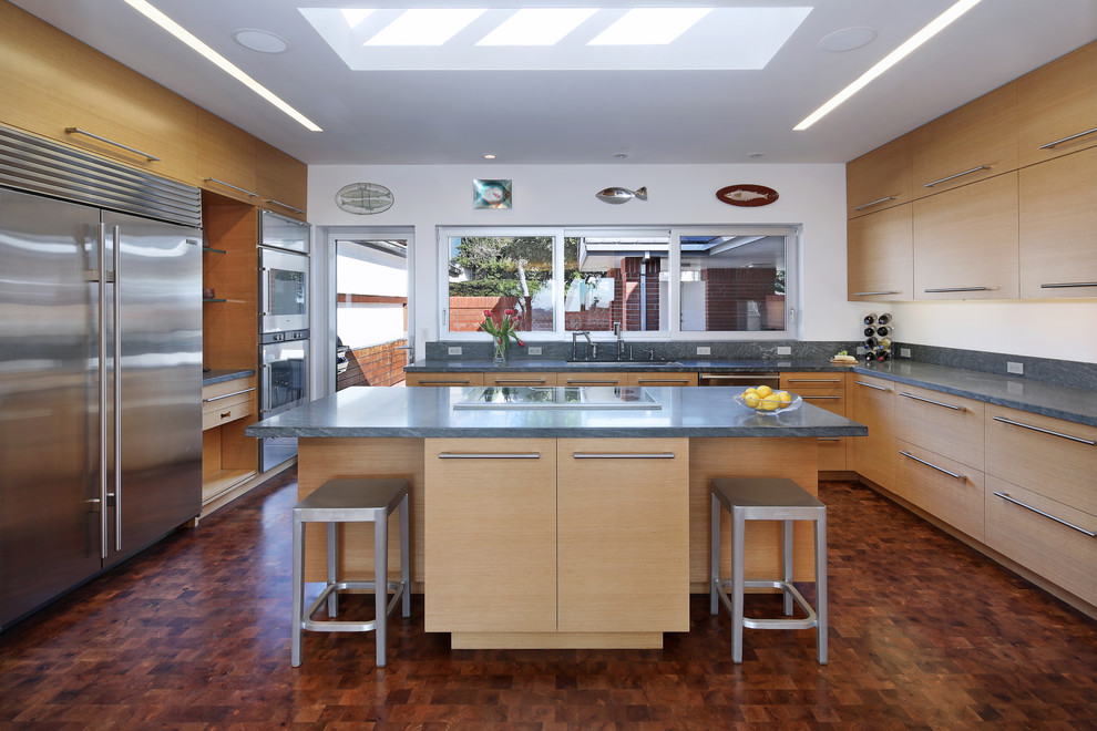 This is an example of a contemporary kitchen in Orange County with a submerged sink, flat-panel cabinets, light wood cabinets, grey splashback, stainless steel appliances, an island, brown floors and granite worktops.