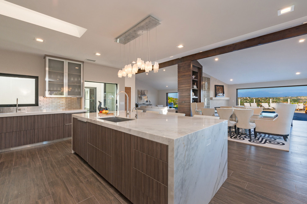 Example of a mid-sized trendy ceramic tile and brown floor eat-in kitchen design in Orange County with an undermount sink, flat-panel cabinets, dark wood cabinets, marble countertops, metallic backsplash, subway tile backsplash, paneled appliances and an island