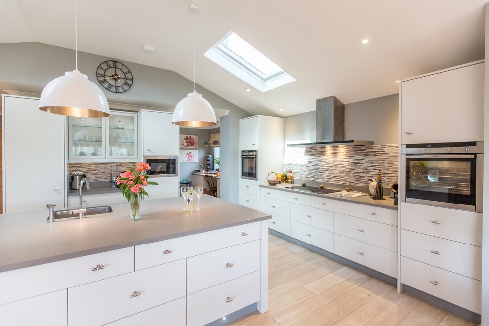 Photo of a medium sized contemporary kitchen in Other with flat-panel cabinets, white cabinets, light hardwood flooring, an island, beige floors, a single-bowl sink, multi-coloured splashback, matchstick tiled splashback and stainless steel appliances.