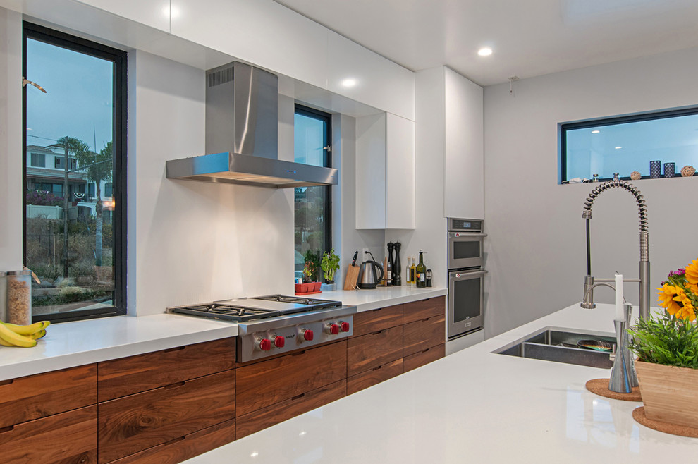 Inspiration for a medium sized modern galley enclosed kitchen in San Diego with flat-panel cabinets, white cabinets, engineered stone countertops, stainless steel appliances, cement flooring, an island and grey floors.