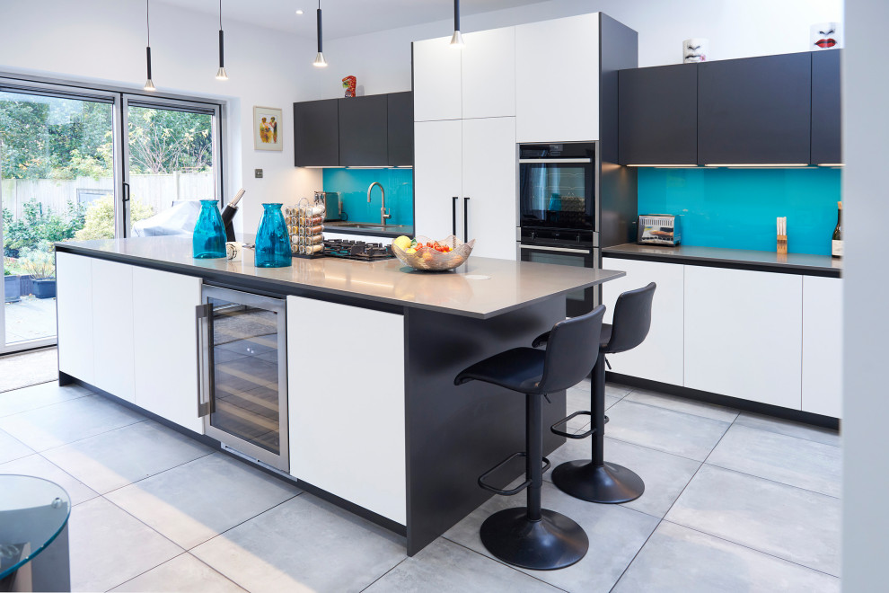 Inspiration for a contemporary galley kitchen in London with a submerged sink, flat-panel cabinets, white cabinets, blue splashback, glass sheet splashback, black appliances, an island, grey floors and grey worktops.