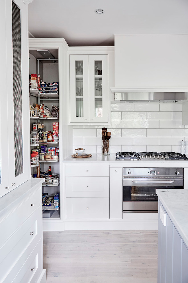 Inspiration for a mid-sized timeless u-shaped light wood floor kitchen pantry remodel in Sydney with a farmhouse sink, shaker cabinets, white cabinets, marble countertops, white backsplash, subway tile backsplash, stainless steel appliances and an island