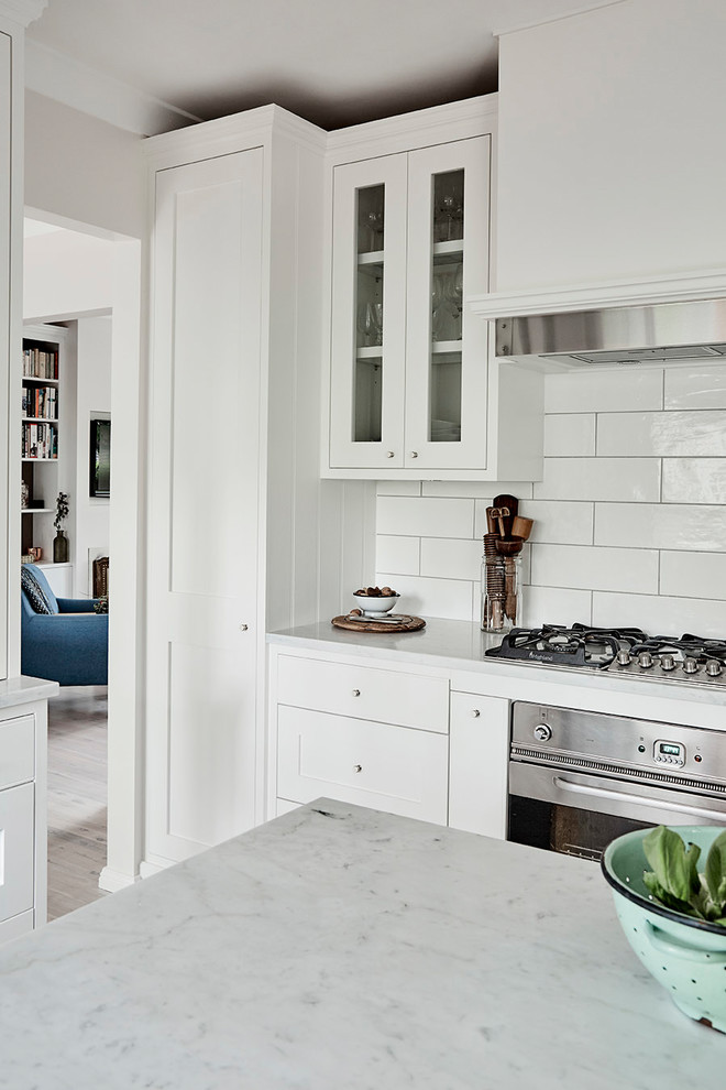 Mid-sized elegant u-shaped light wood floor kitchen pantry photo in Sydney with a farmhouse sink, shaker cabinets, white cabinets, marble countertops, white backsplash, subway tile backsplash, stainless steel appliances and an island