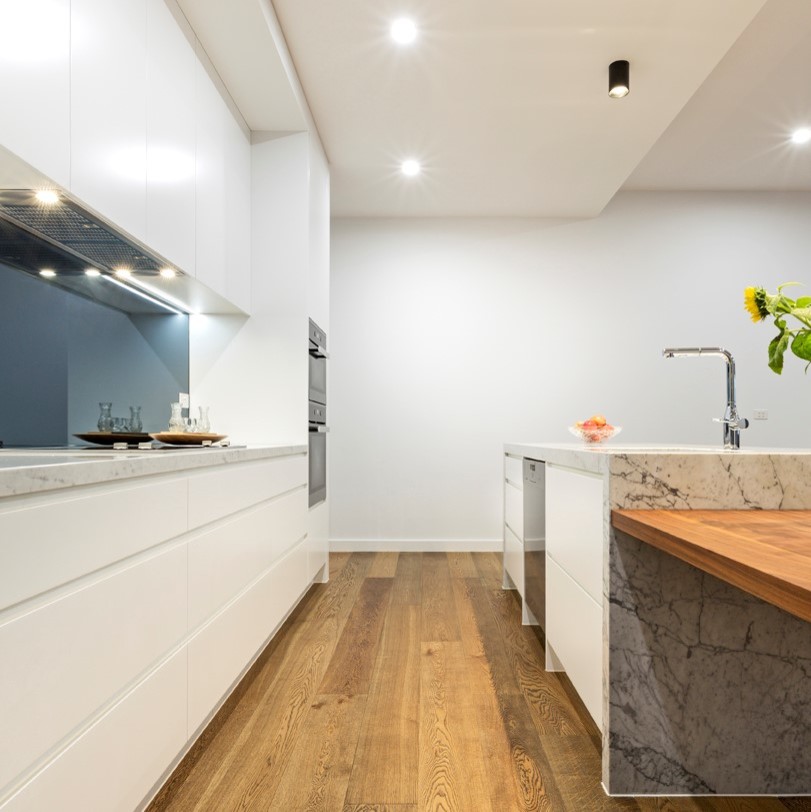 Exempel på ett mellanstort modernt vit linjärt vitt kök och matrum, med en undermonterad diskho, släta luckor, vita skåp, marmorbänkskiva, grått stänkskydd, spegel som stänkskydd, svarta vitvaror, mellanmörkt trägolv, en köksö och flerfärgat golv