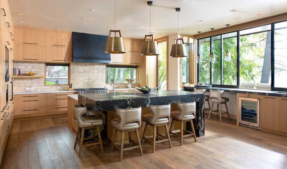 Moderne Küche in U-Form mit flächenbündigen Schrankfronten, hellbraunen Holzschränken, Küchenrückwand in Beige, braunem Holzboden, Kücheninsel, braunem Boden und schwarzer Arbeitsplatte in Sonstige