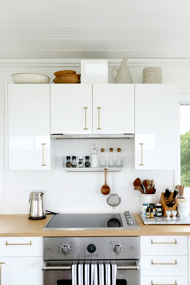Imagen de cocina actual con armarios con paneles lisos, puertas de armario blancas, salpicadero blanco, electrodomésticos de acero inoxidable y encimera de madera