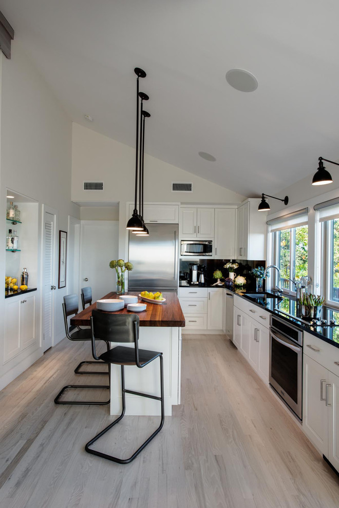 Inspiration for a mid-sized contemporary l-shaped light wood floor open concept kitchen remodel in New York with an undermount sink, flat-panel cabinets, white cabinets, granite countertops, black backsplash, stone slab backsplash, stainless steel appliances and an island