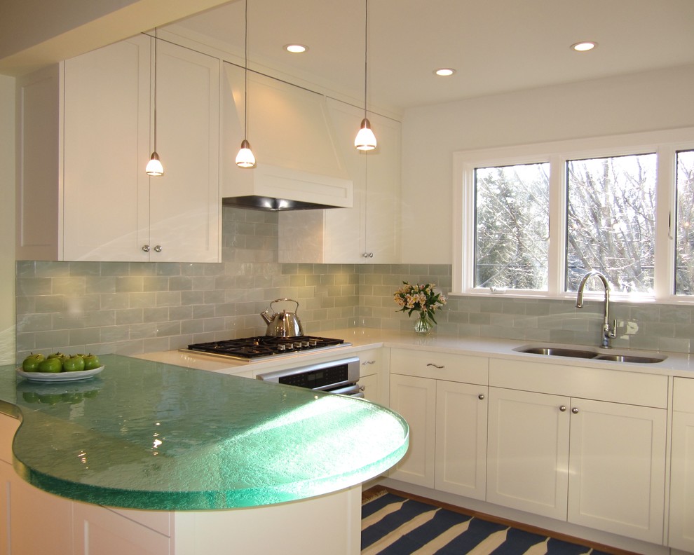 Mid-sized beach style l-shaped light wood floor kitchen photo in New York with a double-bowl sink, shaker cabinets, white cabinets, green backsplash, glass tile backsplash, stainless steel appliances and a peninsula