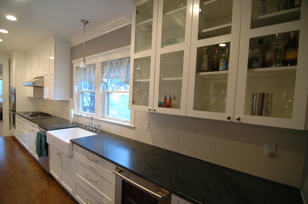 Design ideas for a classic l-shaped kitchen/diner in New York with a belfast sink, shaker cabinets, white cabinets, soapstone worktops, white splashback, metro tiled splashback and stainless steel appliances.