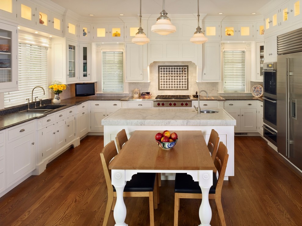 Inredning av ett klassiskt stort kök, med en dubbel diskho, vita skåp, marmorbänkskiva, stänkskydd i stenkakel, rostfria vitvaror, mellanmörkt trägolv och en köksö