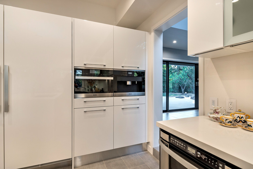This is an example of a large contemporary u-shaped open plan kitchen in San Francisco with a built-in sink, flat-panel cabinets, dark wood cabinets, engineered stone countertops, white splashback, stainless steel appliances, an island, ceramic flooring and grey floors.