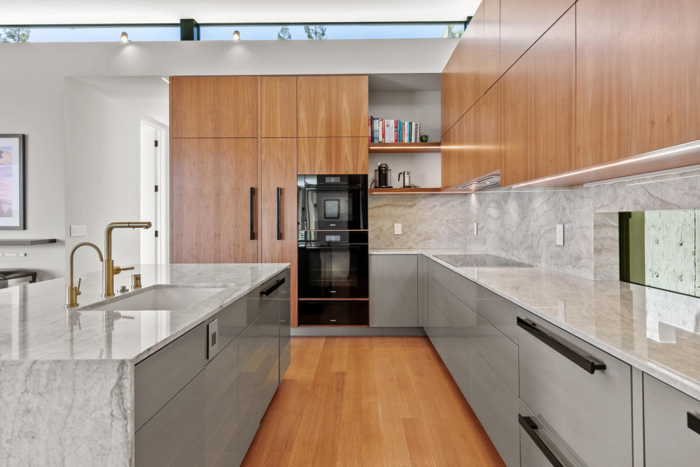 Bild på ett mellanstort funkis grå grått kök, med en undermonterad diskho, släta luckor, skåp i mellenmörkt trä, bänkskiva i kvartsit, grått stänkskydd, stänkskydd i sten, svarta vitvaror, mellanmörkt trägolv, en köksö och brunt golv