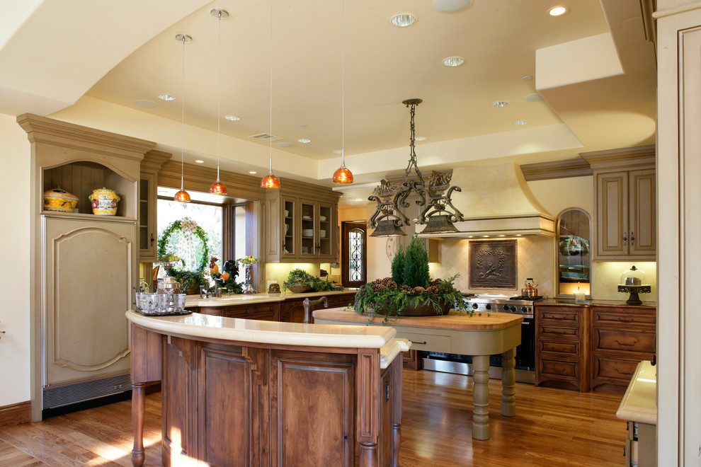 Example of a mid-sized tuscan u-shaped medium tone wood floor open concept kitchen design in San Francisco with an undermount sink, raised-panel cabinets, medium tone wood cabinets, beige backsplash, stone tile backsplash, stainless steel appliances and two islands