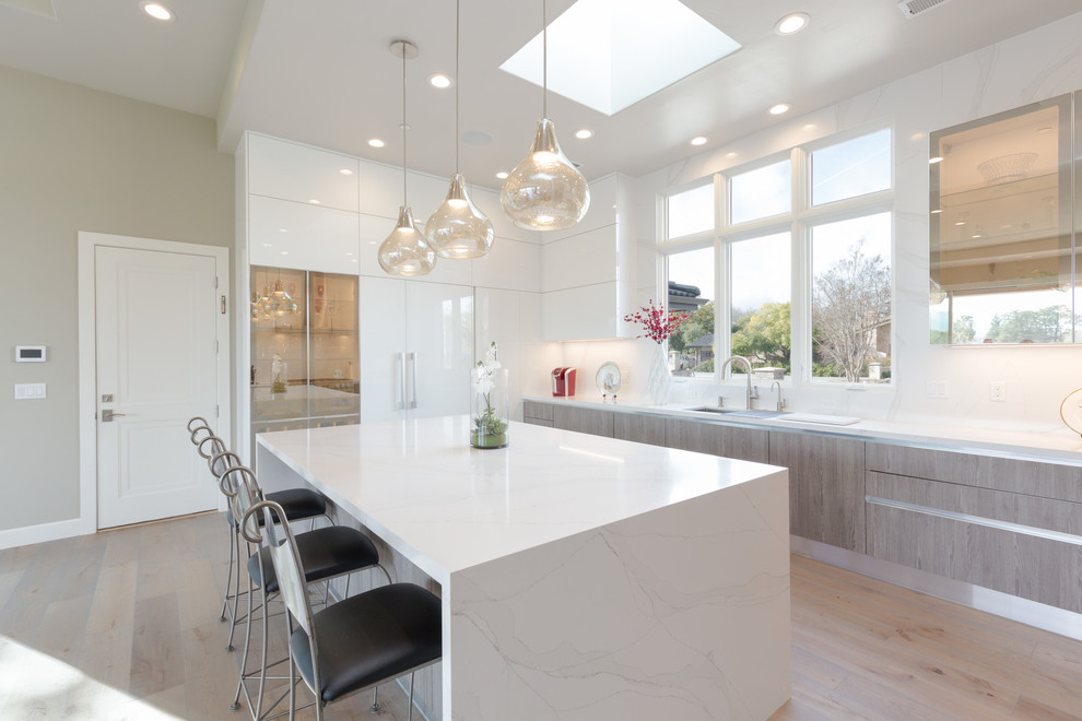 Modern inredning av ett stort kök, med en undermonterad diskho, släta luckor, vita skåp, bänkskiva i kvarts, vitt stänkskydd, stänkskydd i sten, rostfria vitvaror, ljust trägolv, en köksö och brunt golv