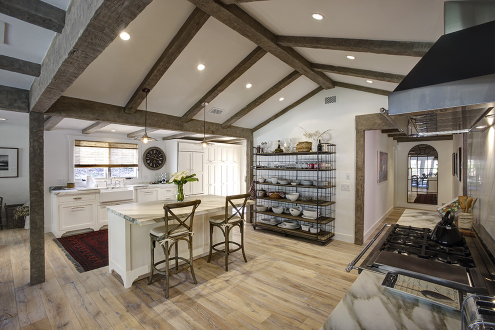 Inspiration for a transitional galley light wood floor open concept kitchen remodel in Santa Barbara with a farmhouse sink, shaker cabinets, white cabinets, marble countertops, white backsplash, stone slab backsplash, stainless steel appliances and an island