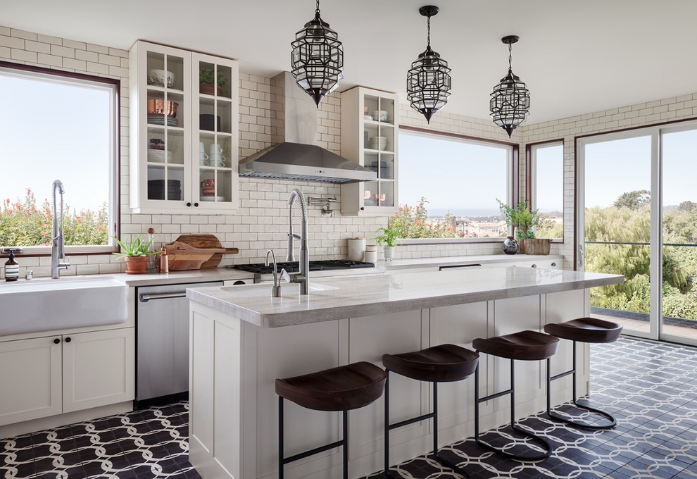 Inspiration for a mediterranean galley kitchen in San Francisco with a belfast sink, shaker cabinets, white cabinets, white splashback, metro tiled splashback, stainless steel appliances, cement flooring, an island and black floors.