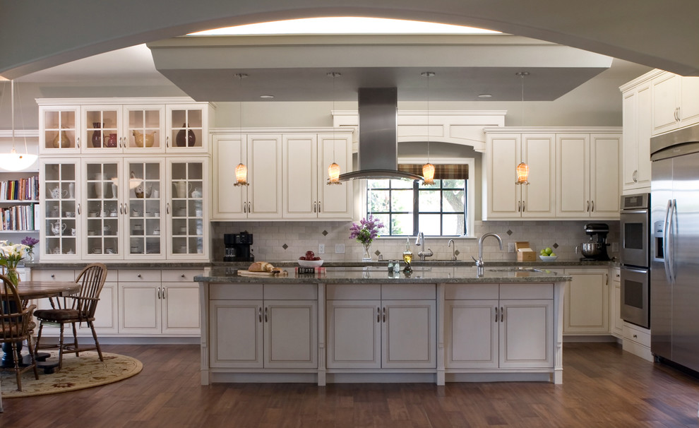 Exempel på ett klassiskt kök, med luckor med glaspanel, rostfria vitvaror, vita skåp, vitt stänkskydd och granitbänkskiva