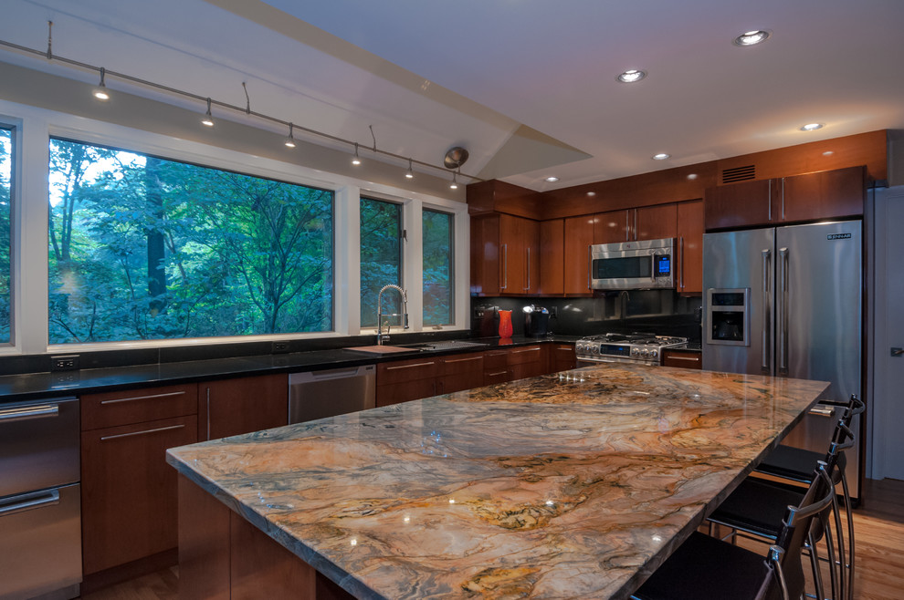 This is an example of an expansive contemporary l-shaped kitchen/diner in DC Metro with a submerged sink, flat-panel cabinets, medium wood cabinets, granite worktops, black splashback, stone slab splashback, stainless steel appliances, medium hardwood flooring and an island.
