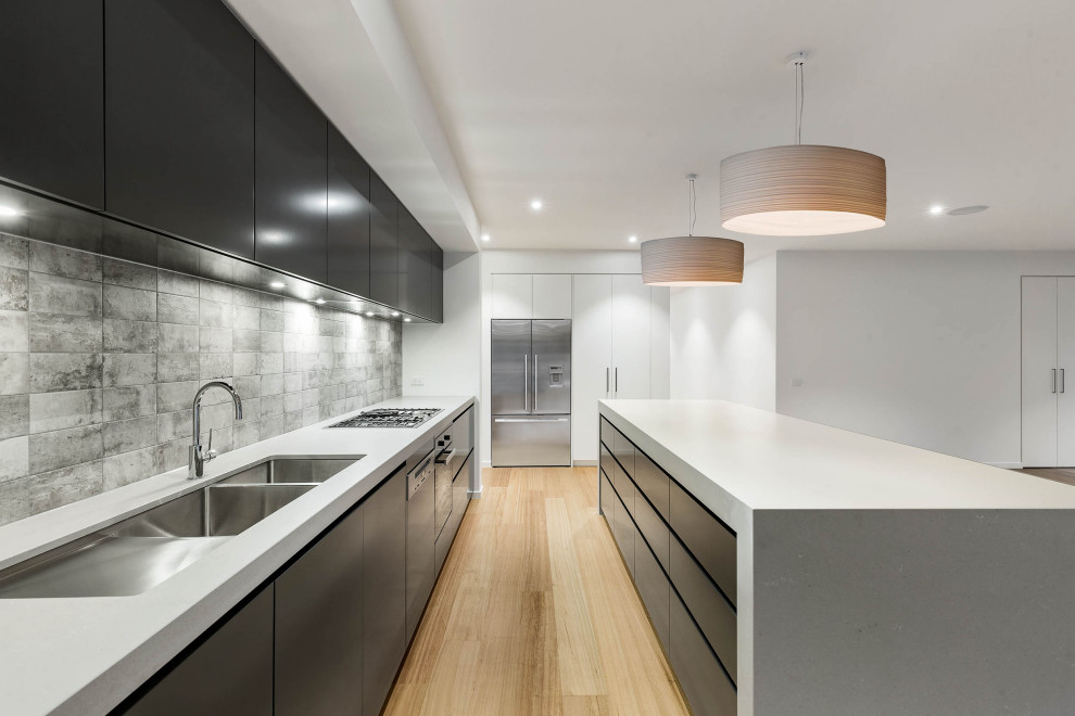 Immagine di una cucina moderna con lavello sottopiano, ante lisce, ante nere, paraspruzzi grigio, elettrodomestici in acciaio inossidabile, parquet chiaro, pavimento beige e top bianco