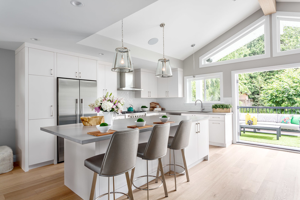 Eat-in kitchen - mid-sized transitional l-shaped medium tone wood floor eat-in kitchen idea in Vancouver with a double-bowl sink, flat-panel cabinets, white cabinets, quartzite countertops, white backsplash, subway tile backsplash, stainless steel appliances and an island