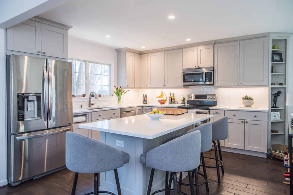 Kitchen - mid-sized transitional l-shaped dark wood floor and brown floor kitchen idea in DC Metro with an undermount sink, gray cabinets, quartz countertops, white backsplash, subway tile backsplash, stainless steel appliances, an island, white countertops and shaker cabinets