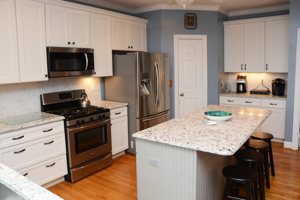 Bild på ett stort vintage kök, med en undermonterad diskho, luckor med infälld panel, vita skåp, bänkskiva i kvarts, vitt stänkskydd, stänkskydd i porslinskakel, rostfria vitvaror, ljust trägolv och en köksö