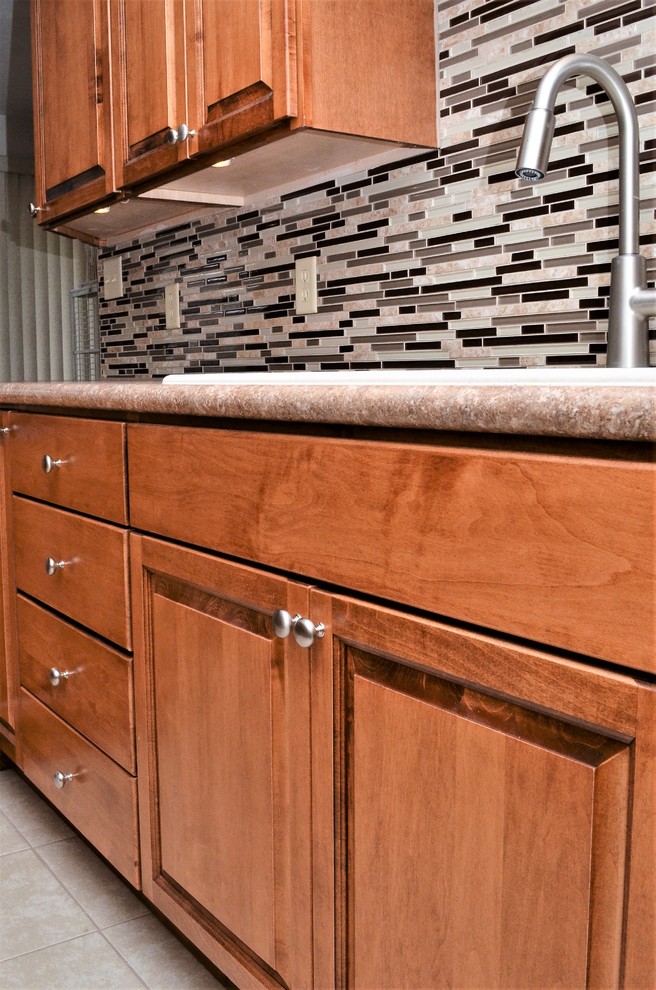 Example of a mid-sized transitional l-shaped ceramic tile and beige floor eat-in kitchen design in Other with a drop-in sink, raised-panel cabinets, medium tone wood cabinets, laminate countertops, multicolored backsplash, matchstick tile backsplash, stainless steel appliances, a peninsula and beige countertops