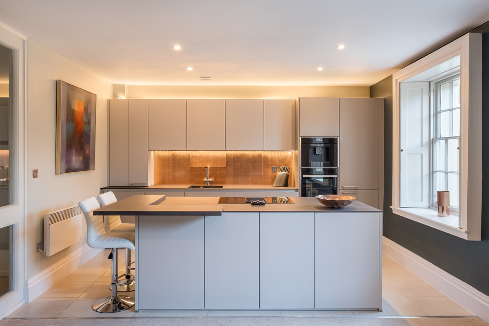 Exemple d'une cuisine parallèle tendance de taille moyenne avec un placard à porte plane, des portes de placard grises, une crédence métallisée, un électroménager noir, îlot et un sol blanc.