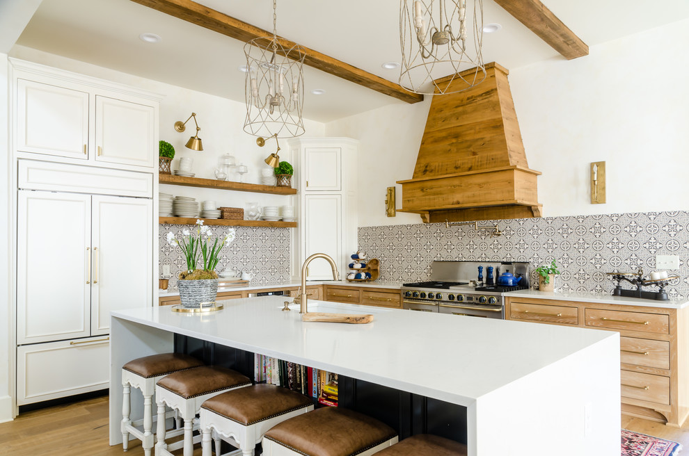 Bild på ett lantligt vit vitt l-kök, med en undermonterad diskho, luckor med infälld panel, skåp i ljust trä, flerfärgad stänkskydd, integrerade vitvaror, mellanmörkt trägolv, en köksö och brunt golv