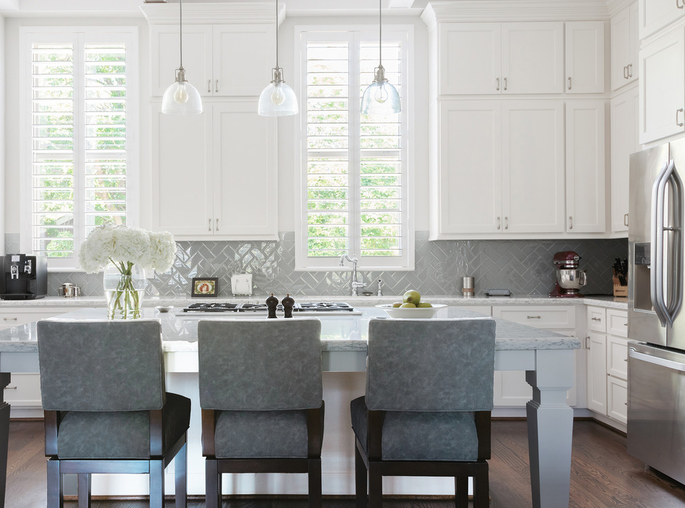 Eat-in kitchen - mid-sized traditional l-shaped medium tone wood floor and brown floor eat-in kitchen idea in Houston with a drop-in sink, flat-panel cabinets, white cabinets, marble countertops, gray backsplash, glass tile backsplash, stainless steel appliances and an island