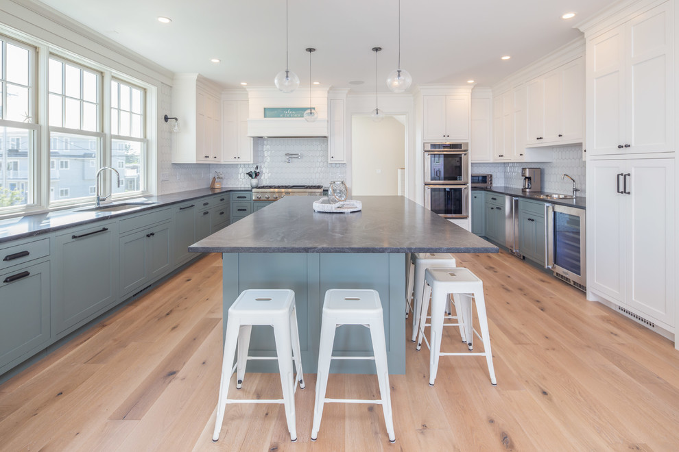 Maritim inredning av ett grå grått kök, med en undermonterad diskho, skåp i shakerstil, blå skåp, vitt stänkskydd, rostfria vitvaror, ljust trägolv, en köksö, beiget golv och granitbänkskiva