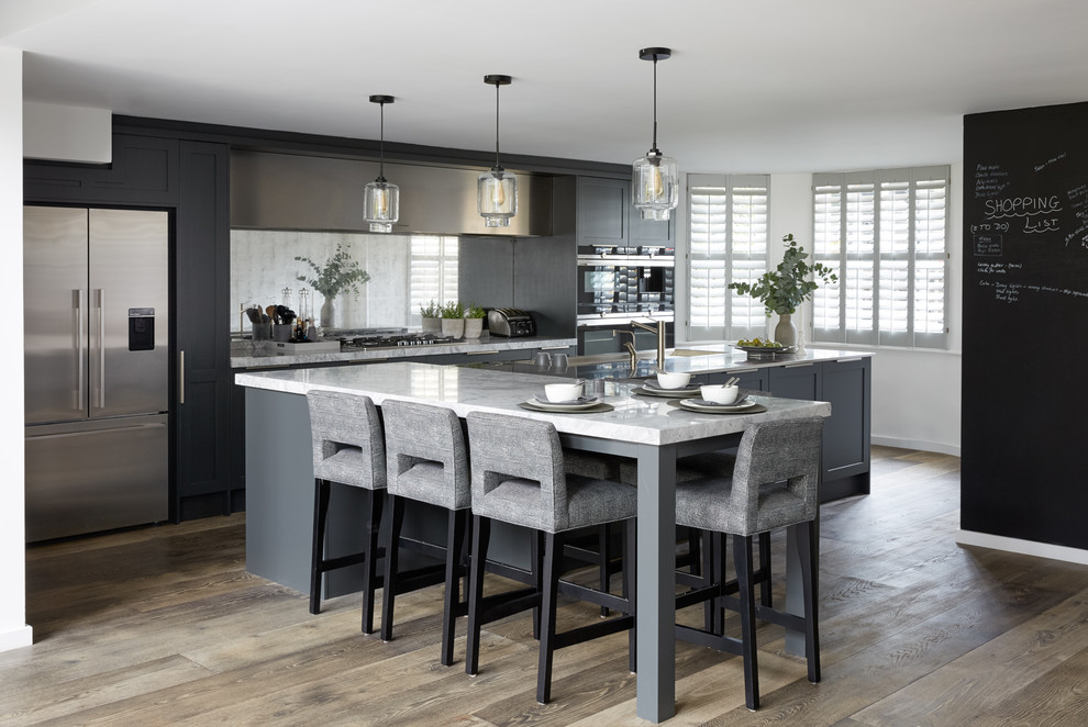 Design ideas for a large contemporary kitchen/diner in London with blue cabinets, marble worktops, metallic splashback, mirror splashback, stainless steel appliances, medium hardwood flooring, multiple islands, white worktops, a submerged sink, shaker cabinets and beige floors.