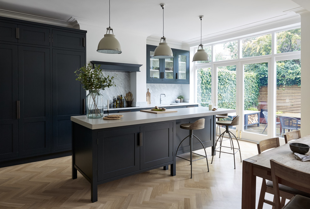 Inspiration for a large contemporary galley medium tone wood floor eat-in kitchen remodel in London with a drop-in sink, recessed-panel cabinets, blue cabinets, an island, white countertops, solid surface countertops, white backsplash, marble backsplash and paneled appliances
