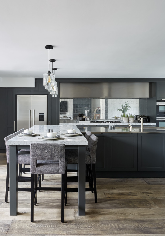 Design ideas for a large contemporary l-shaped kitchen/diner in London with a built-in sink, recessed-panel cabinets, blue cabinets, marble worktops, metallic splashback, mirror splashback, stainless steel appliances, medium hardwood flooring, multiple islands and white worktops.