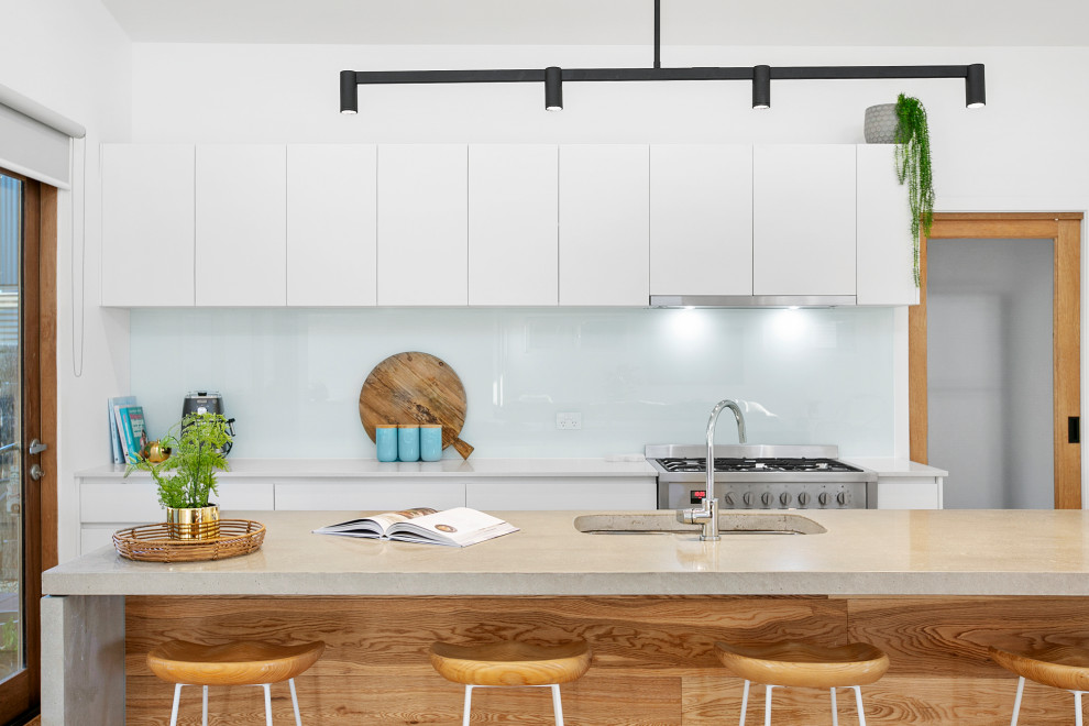 Foto på ett mellanstort funkis grå kök, med en undermonterad diskho, släta luckor, vita skåp, bänkskiva i betong, vitt stänkskydd, glaspanel som stänkskydd, rostfria vitvaror, mellanmörkt trägolv, en köksö och beiget golv