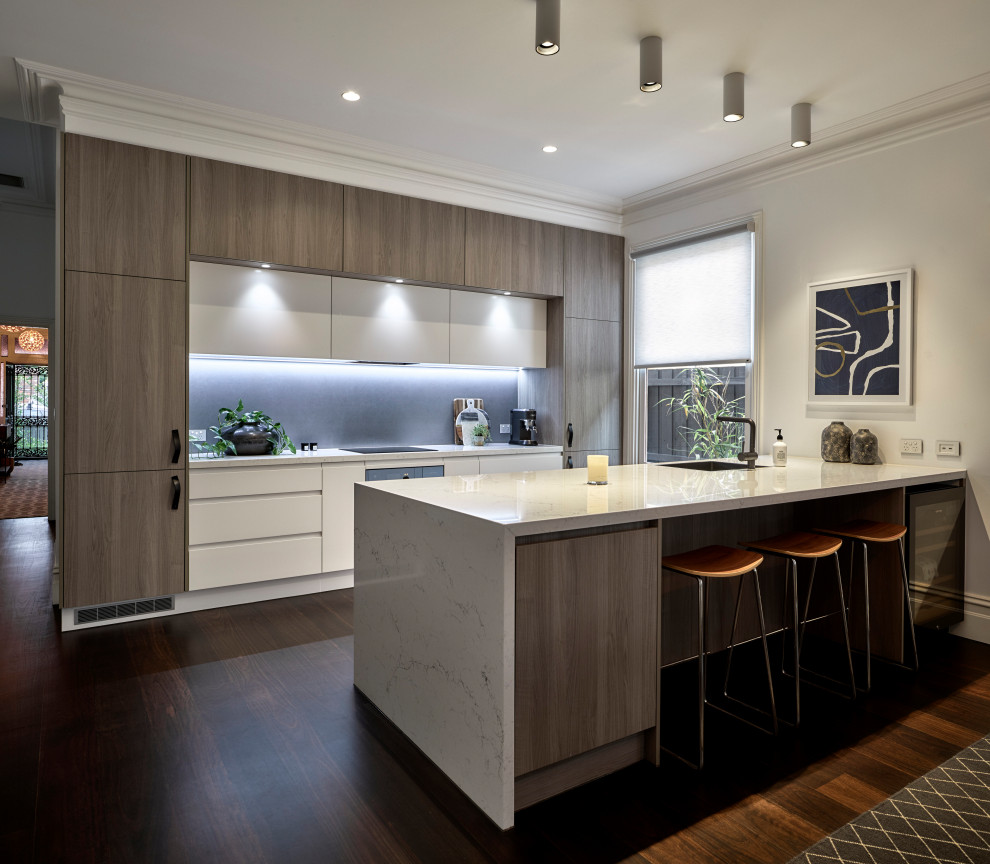Example of a mid-sized trendy galley brown floor kitchen design in Melbourne with an undermount sink, flat-panel cabinets, white cabinets, black backsplash, paneled appliances, a peninsula and white countertops
