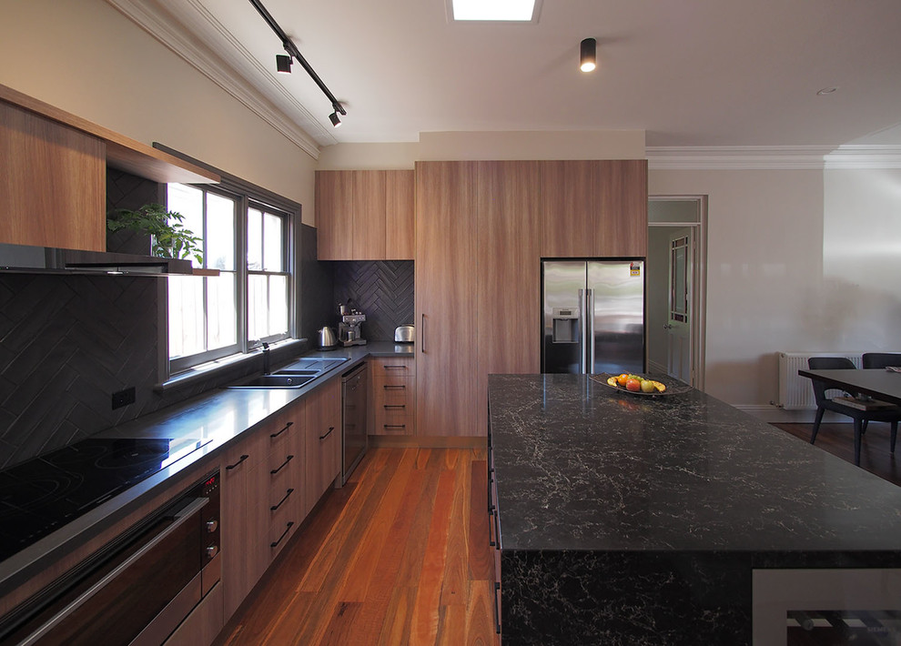 Example of a mid-sized trendy l-shaped medium tone wood floor kitchen pantry design in Melbourne with a double-bowl sink, medium tone wood cabinets, quartz countertops, black backsplash, ceramic backsplash, black appliances and an island