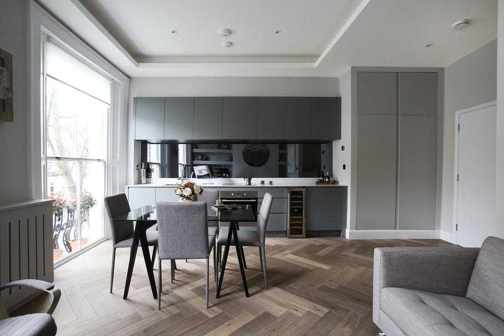 Offene, Einzeilige Moderne Küche ohne Insel mit Unterbauwaschbecken, flächenbündigen Schrankfronten, grauen Schränken, Küchenrückwand in Schwarz und hellem Holzboden in London