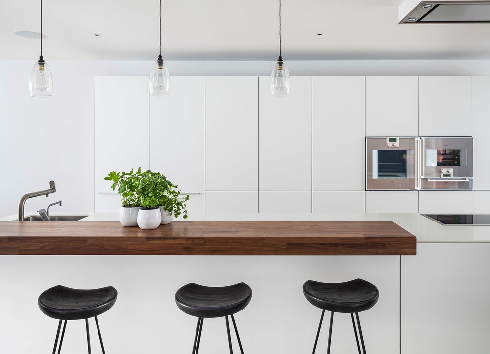 Einzeilige Moderne Küche mit flächenbündigen Schrankfronten, weißen Schränken, Kücheninsel, Unterbauwaschbecken, Mineralwerkstoff-Arbeitsplatte und Küchengeräten aus Edelstahl in London