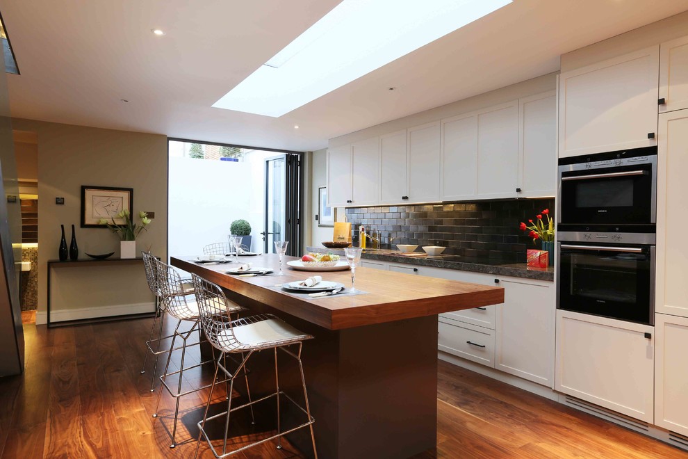 This is an example of a medium sized contemporary single-wall kitchen in London with recessed-panel cabinets, medium hardwood flooring, an island and brown floors.