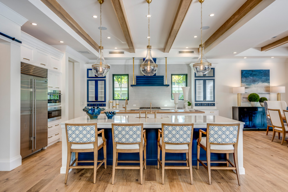 Inspiration for a large nautical open plan kitchen in Miami with a belfast sink, shaker cabinets, white cabinets, engineered stone countertops, grey splashback, porcelain splashback, stainless steel appliances, light hardwood flooring, multiple islands, brown floors and white worktops.