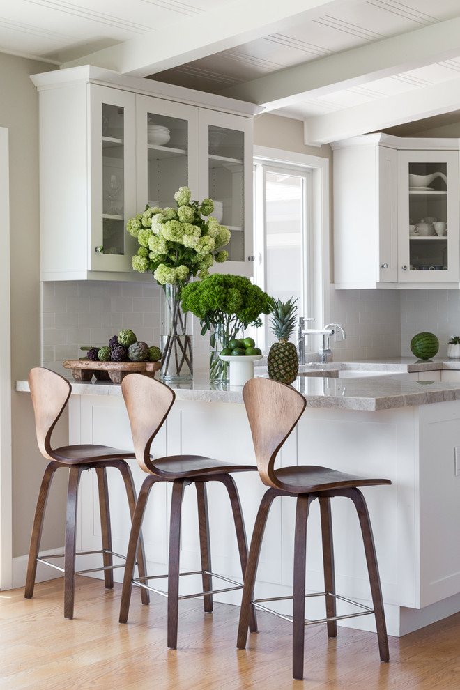 Example of a mid-sized transitional u-shaped light wood floor and brown floor eat-in kitchen design in San Francisco with glass-front cabinets, white cabinets, subway tile backsplash, a peninsula, granite countertops, white backsplash, a farmhouse sink and stainless steel appliances