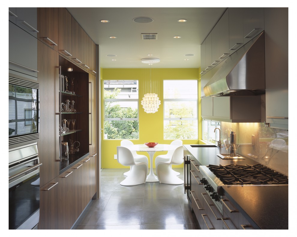 Cette photo montre une cuisine américaine moderne en bois foncé avec un électroménager en acier inoxydable, un placard à porte plane, une crédence blanche et une crédence en dalle de pierre.