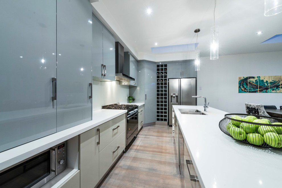 Example of a mid-sized trendy l-shaped light wood floor eat-in kitchen design in Melbourne with an undermount sink, flat-panel cabinets, gray cabinets, quartz countertops, white backsplash, glass sheet backsplash, stainless steel appliances and an island